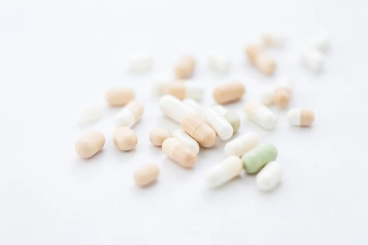 Pílulas e cápsulas de vitaminas em tons de bege e branco, em close-up.