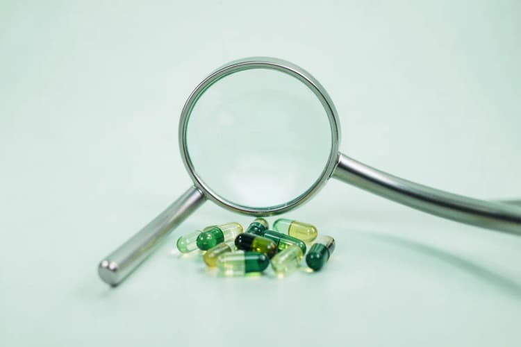 Uma lupa examinando várias cápsulas de suplementos.