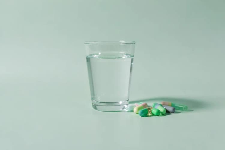 Um copo de água com várias cápsulas de suplementos ao lado.