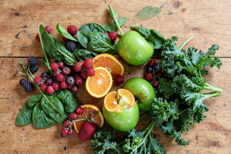 Uma seleção de frutas frescas e vegetais dispostos artisticamente em uma superfície de madeira rústica.