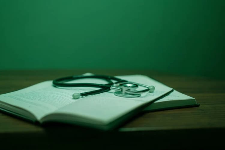Um estetoscópio repousando sobre um livro aberto de medicina em uma mesa de madeira.