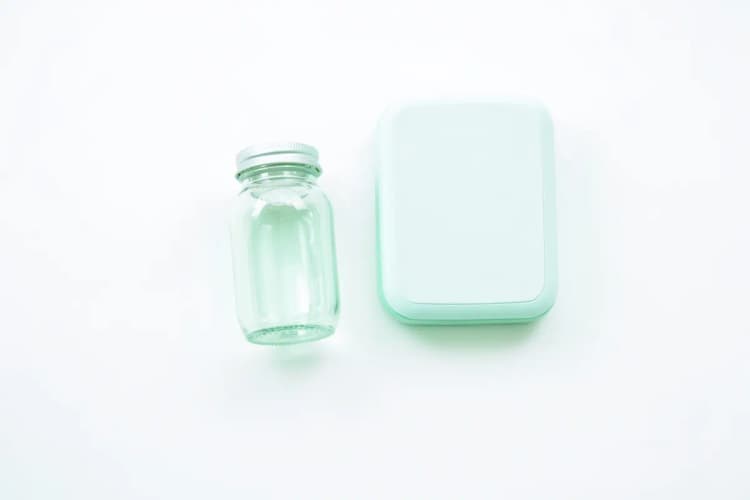 Uma garrafa de suplemento vitamínico vazia e uma balança de cozinha sobre uma superfície branca.