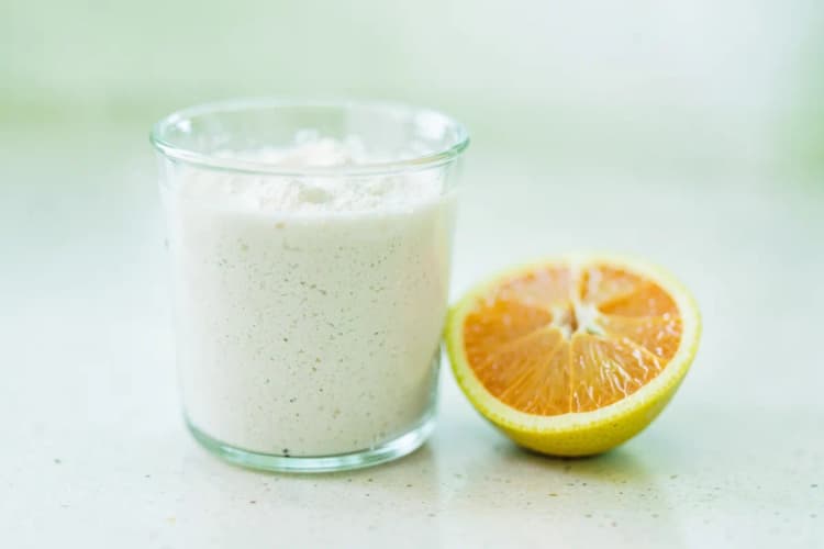 Copo com colágeno hidrolisado em pó dissolvido e uma fruta cortada ao lado