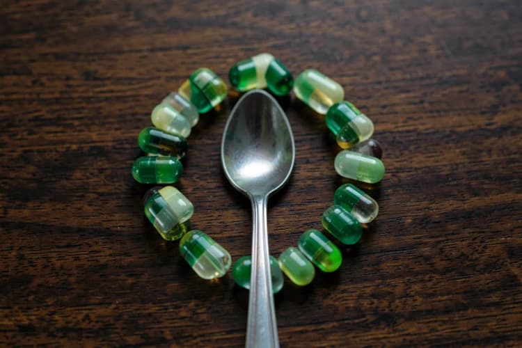 Um conjunto de cápsulas de colágeno dispostas em círculo sobre uma superfície de madeira escura, com uma colher de metal no centro.