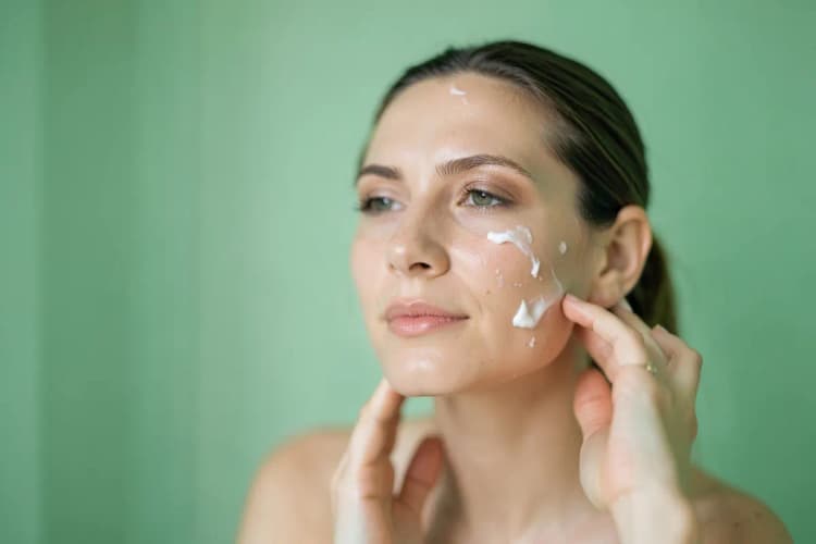 Mulher aplicando creme no rosto com as mãos, com foco na pele radiante.