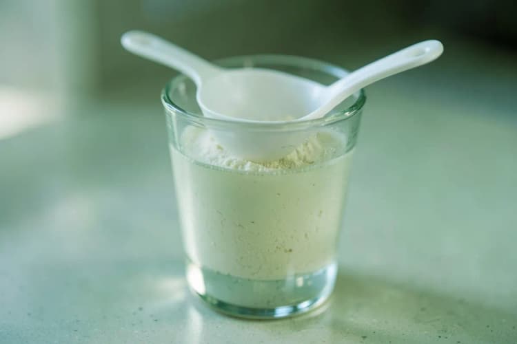 Um copo com colágeno Verisol dissolvido em água, com uma colher dosadora ao lado.