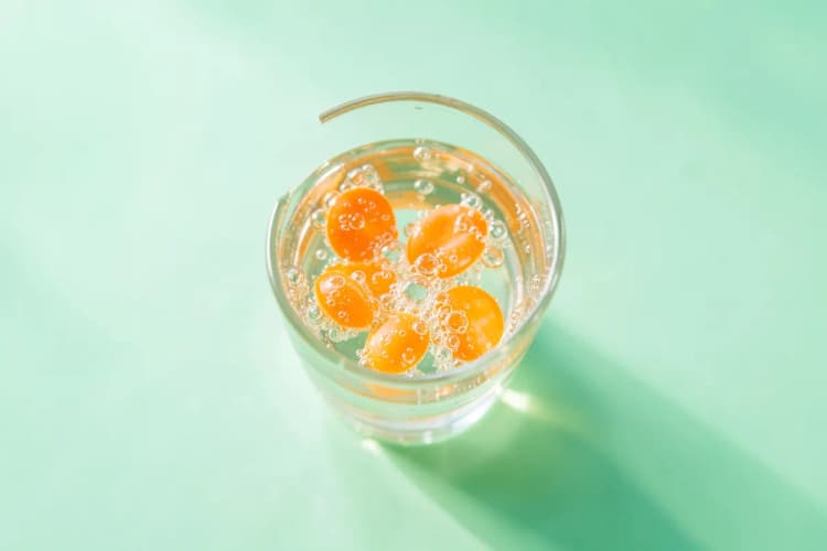 Um close-up de comprimidos efervescentes de vitamina C dissolvendo-se em um copo de água, criando bolhas efervescentes.