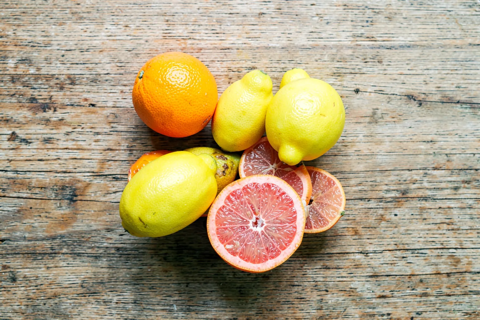 Uma tigela de frutas cítricas frescas e vibrantes, incluindo laranjas, limões e toranjas, dispostas artisticamente sobre uma superfície de madeira rústica.