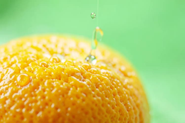 Um close-up extremo de gotas de água brilhantes caindo sobre a casca texturizada de uma laranja suculenta, destacando a frescura e a vitalidade.