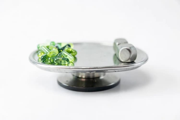 Uma balança de precisão com cápsulas de ômega 3 de um lado e um peso do outro, em um fundo branco limpo.
