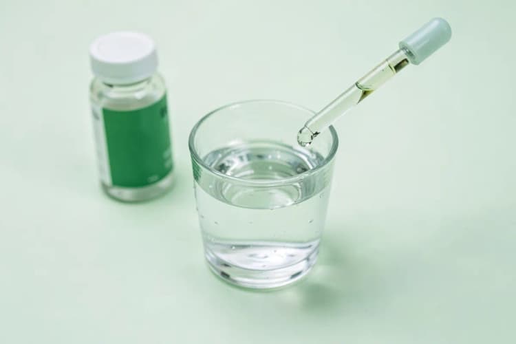 Um copo d'água sendo enchido a partir de um conta-gotas, com o frasco de melatonina ao lado