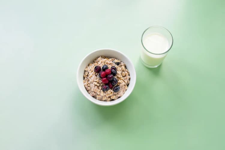 Uma tigela de cereais com frutas vermelhas e um copo de leite ao lado, em uma mesa de café da manhã