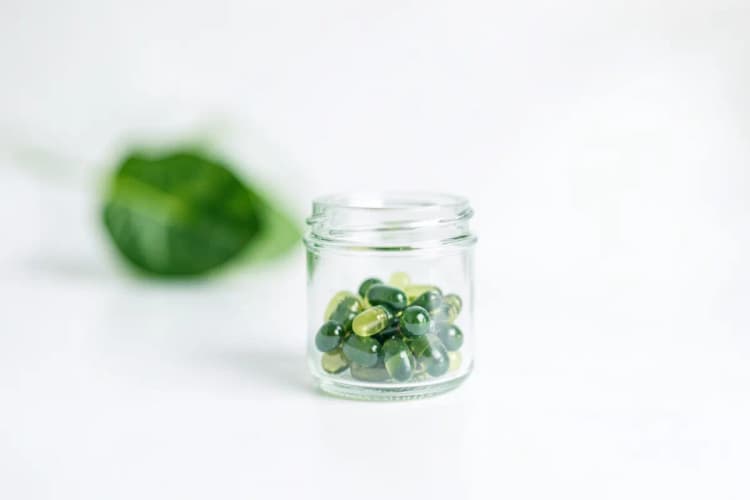 Cápsulas de ômega 3 em um recipiente de vidro transparente com um fundo branco e uma folha verde desfocada