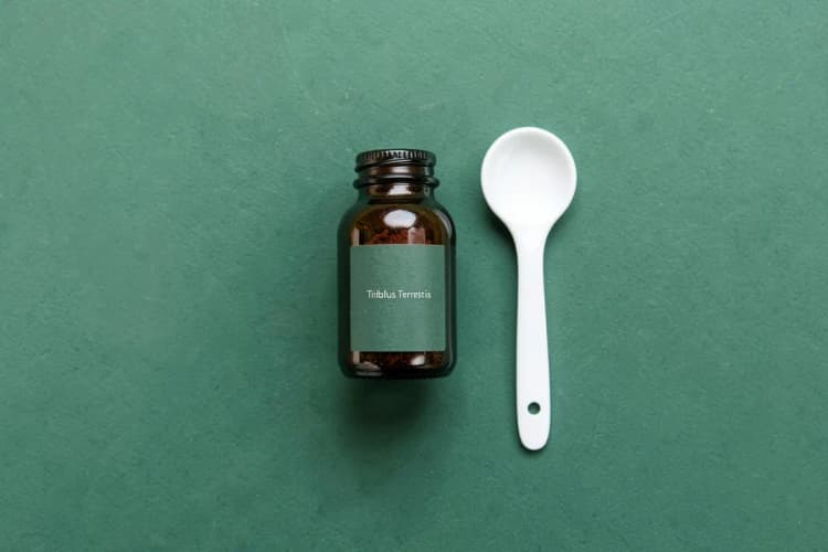 Um frasco de tribulus terrestris em pó com a tampa aberta e uma colher dosadora ao lado.