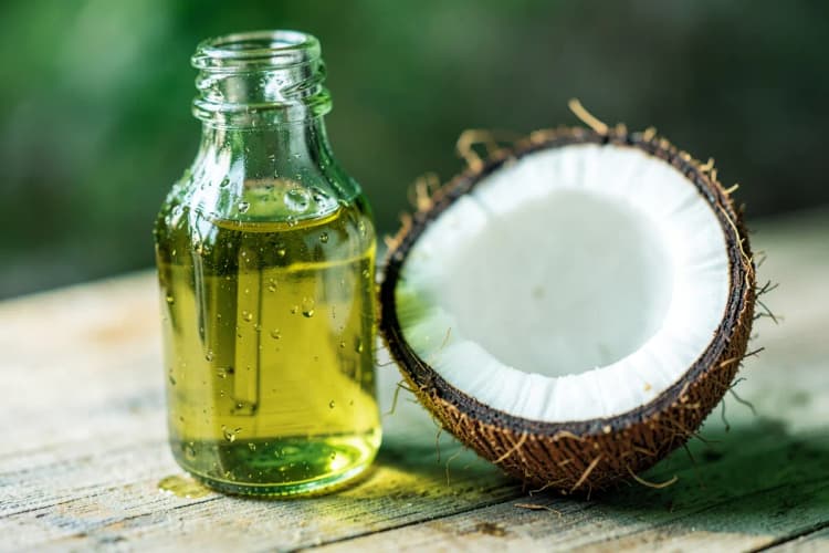 Um frasco de vidro com óleo de coco e um coco partido ao meio em uma superfície de madeira clara.