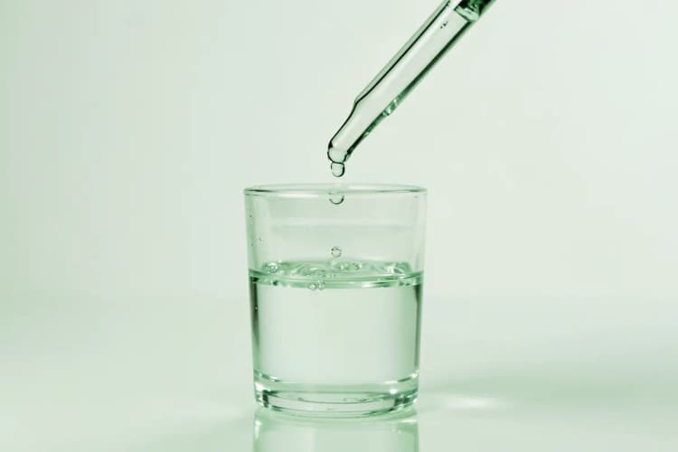 Gotas de vitamina C caindo de um conta-gotas em um copo com água.