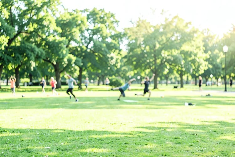 Pessoas praticando atividades físicas ao ar livre, como corrida e yoga, em um parque ensolarado.