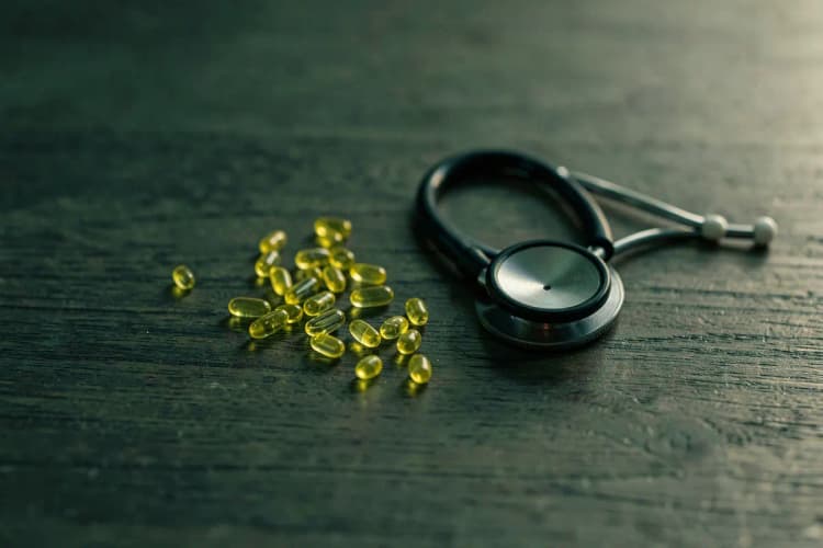 Cápsulas de vitamina D e um estetoscópio sobre um fundo de madeira.